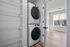 Bright laundry room with sleek stacked washer and dryer next to spacious shelving in a modern apartment.