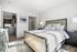 Bright and inviting bedroom with elegant decor, featuring a plush bed, modern furniture, and a view into a sleek kitchen with stylish cabinetry.