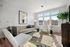 Bright, modern living room featuring chic decor, a plush beige couch, stylish armchairs, and a vibrant patterned rug, illuminated by natural light through large windows.