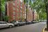 Charming brick apartment building nestled among lush trees, offering a serene urban living experience with convenient street parking.