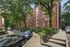 Charming brick apartment building surrounded by lush green trees and a well-maintained pathway, offering a serene urban living experience.