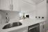 Modern kitchen with sleek stainless-steel sink and dishwasher, opening into a bright living area with a large window view.