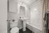 Elegant bathroom featuring a chic marble-tiled bathtub, modern pedestal sink, and soft lighting for a serene atmosphere.