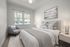 Bright and cozy bedroom with modern decor, featuring a plush bed with elegant pillows, an inviting armchair, and soft natural light through large windows.