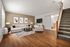 Inviting living room with modern decor, including a spacious sectional sofa, stylish art, and a cozy ambiance, complemented by warm wooden floors and plush carpeted stairs.