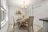 Bright dining area featuring a chic round wooden table set for four, under elegant pendant lighting, complemented by soft natural light from wide windows.