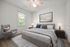 Contemporary bedroom with plush gray bedding, elegant armchair, and modern art. Light-filled space with hardwood floors and stylish decor.