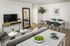 Modern living room with sleek decor, featuring a comfortable gray sofa, stylish coffee tables, and a large mirror enhancing the open space. A chic dining area with blue chairs and elegant art add sophistication.