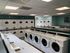 Modern laundry room with multiple washers and dryers, teal accents, and efficient layout.