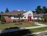 Charming brick building with lush landscaping and vibrant flower beds, featuring a welcoming red door entrance and clear blue skies.