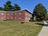 Charming brick apartment building with lush green lawns and mature trees, offering a peaceful and welcoming atmosphere.