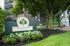Charming Canterbury Place exterior showcasing lush greenery, blooming flowers, and inviting benches under a canopy of trees.