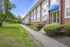Charming brick apartment building with blue awnings, surrounded by lush greenery and a well-kept lawn, offering a serene living environment.