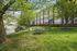 Charming residential building with lush green surroundings, featuring a peaceful sitting area and vibrant trees, perfect for relaxation.
