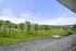 Serene outdoor view from apartment balcony showcasing lush green landscape, vibrant trees, and spacious parking area under a clear blue sky.