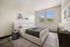 Elegant bedroom with cozy beige bed, stylish modern decor, and large window offering a serene green view.
