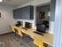 Modern communal workspace featuring sleek computers, vibrant yellow chairs, and ample cabinetry in a bright, inviting setting.