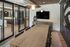 Elegant dining room with a modern wooden table, stylish pendant lighting, and floor-to-ceiling glass doors leading to a sleek kitchen area.