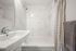 Elegant bathroom featuring marble tiles, a sleek white basin, and a cozy bathtub with artistic shower curtain.