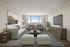 Elegant living room with plush grey sofa, modern armchairs, and floor-to-ceiling windows offering scenic views. Stylish decor and ample natural light create a welcoming atmosphere.