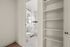 Modern bathroom with sleek white tiles, a stylish round mirror, and an adjacent open shelving unit for ample storage.