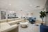 Contemporary living area with elegant beige sectional, modern blue chairs, a stylish round coffee table, and a sleek kitchen in the background.