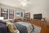 Elegant bedroom with large windows, cozy seating, stylish wooden flooring, and modern entertainment unit.