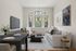 Elegant living room with modern decor, featuring a plush gray sofa, sleek black dining table, and large arched windows offering a charming outdoor view.