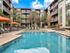Modern apartment complex with a stunning swimming pool, surrounded by stylish lounge chairs and vibrant orange umbrellas, offering a luxurious outdoor leisure experience.