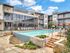 Luxurious apartment complex featuring a sparkling pool, modern lounge chairs, and elegant architecture under a clear blue sky.