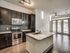 Modern kitchen with sleek dark wood cabinetry, stainless steel appliances, and elegant pendant lighting, leading to a bright living area with large windows.