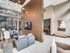 Modern, inviting living space with high ceilings, large windows, and stylish seating area. Warm lighting creates a cozy ambiance alongside sleek wall accents and contemporary decor.
