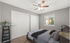 Inviting bedroom with cozy carpeting, stylish ceiling fan, abundant natural light from a large window, and a lush potted plant for a serene ambiance.