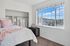 Bright bedroom featuring a cozy bed with pink and white decor, open closet space, and a sunlit window with picturesque views.