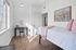 Bright and inviting bedroom with plush carpeting, a cozy bed adorned with soft pink accents, and a stylish desk near a sunlit window, perfect for productivity.