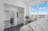 Bright bedroom with a spacious closet, cozy decor, and a breathtaking panoramic window view of the cityscape.