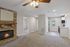 Inviting living room with a cozy stone fireplace, modern ceiling fan, and seamless access to a bright kitchen area featuring sleek appliances and large windows.