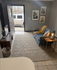 Cozy modern living room featuring a plush blue sofa, textured rug, and elegant wall art, with natural light streaming in through an open door.