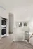 Bright and modern apartment staircase leading down to a stylish entryway, featuring a convenient in-unit stacked washer and dryer, complemented by sleek wood flooring and large, sunlit windows.