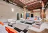 Chic industrial-style lounge with exposed beams and modern seating, featuring vibrant orange accents in a spacious, airy atmosphere.