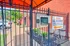 Secure gated entrance with intercom system at vibrant apartment complex, featuring lush greenery and bright orange accents.