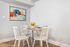 Charming dining nook with a round table set and modern white chairs, accented by vibrant abstract artwork on the wall.
