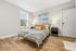 Inviting bedroom with modern decor, featuring a plush bed adorned with striped bedding and vibrant yellow pillows, set against a tranquil wall art. Gleaming wooden floors and ample natural light create a serene ambiance.