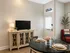 Chic and inviting living area with elegant decor, featuring a stylish TV console, cozy red chair, and a beautifully set dining table for four beneath warm lighting.