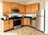 Modern kitchen with stainless steel appliances, wooden cabinetry, and a bright, lemon-themed rug on hardwood floors.