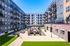 Contemporary apartment complex courtyard with lush green artificial turf, ample seating, and modern architectural design, perfect for community gatherings.