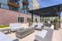 Luxurious outdoor seating area with modern furniture and pergola, featuring lush planters and vibrant urban backdrop.