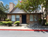 Charming brick home with a dark blue door, nestled among lush greenery and vibrant flowers, exuding cozy curb appeal.