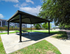 Inviting outdoor pavilion with picnic tables, nestled in a green landscape, adjacent to modern apartment buildings.