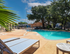 Inviting outdoor pool area with sun loungers, shaded by mature trees, offering a perfect relaxation spot under a clear blue sky.